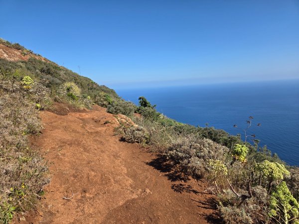 Tramo del sendero rojizo que conduce al mirador de Aguaide con el océano al fondo.